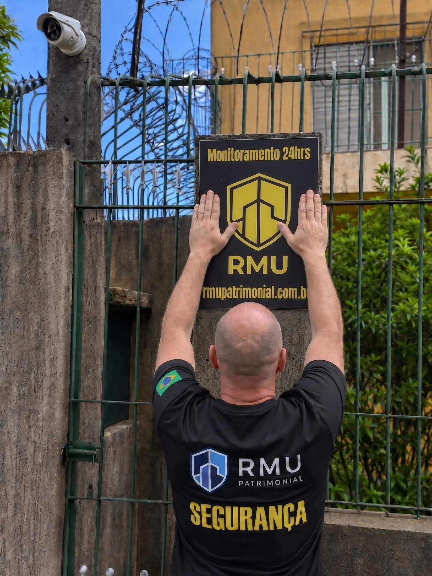 Agente RMU instalando placa de monitoramento 24h em portão residencial
